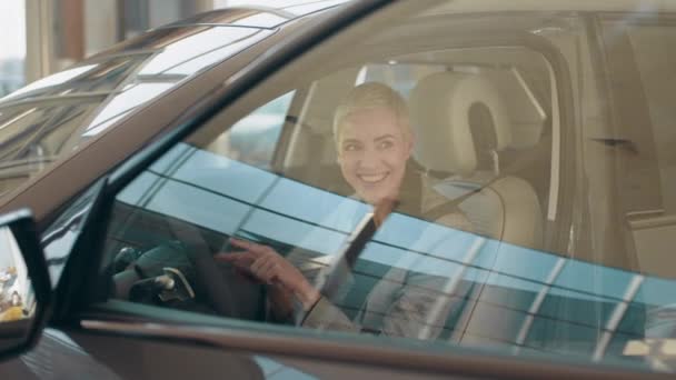 Eko araba satışı konsepti. Otomatik sürüş sistemi olan yeni nesil elektrikli aracın test sürüşü. Çekici beyaz kadın yeni modern arabanın direksiyonunda oturuyor ve kameraya gülümsüyor.. — Stok video