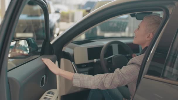 Konsep penjualan mobil Eco. Uji mengemudi kendaraan listrik generasi baru dengan sistem self driving. Wanita Kaukasia yang menarik duduk di belakang kemudi mobil modern baru dan tersenyum di depan kamera. — Stok Video