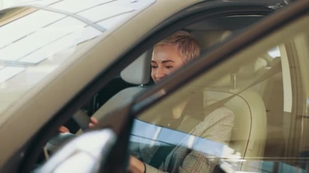 Çekici beyaz kadın yeni modern arabanın direksiyonunda oturuyor ve kameraya gülümsüyor. Eko araba satışı konsepti. Galeride otomatik sürüş sistemi olan yeni nesil elektrikli aracın test sürüşü — Stok video