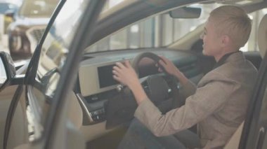 Otomobil galerisi ziyareti sırasında içeriden araba alan mutlu kadın test çekimlerinin yakın çekimi. Otomatik sürüş sistemi olan yeni nesil elektrikli aracın test sürüşü. Direksiyonda oturan kadın.