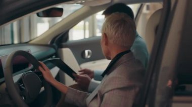 Eko araba satışı konsepti. Çevre dostu ve modern araba alma kavramı. Modern otomobilin içinde oturan sarışın iş kadını gösterge paneli tasarımına bakıyor, yetkili satış müdürüyle konuşuyor..