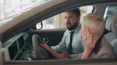 Modern bir otomobilin içinde oturan sarışın iş kadını gösterge paneli tasarımına bakıyor ve yetkili bir galeri müdürüyle konuşuyor. Eko araba satışı konsepti. Çevre dostu ve modern araba satın alma kavramı.