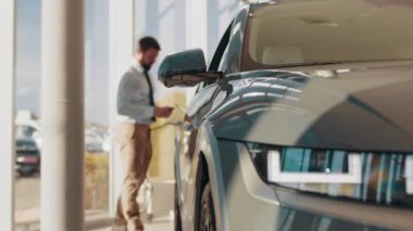 Yakışıklı bir iş adamı elektrikli araba için kablolu yayın tutuyor. Bayilikte beyaz erkek elektrikli otomobilin yanında duruyor. Şarj istasyonunda elektrikli araba şarj ediliyor. Yeni arabasını şarj etme işlemi