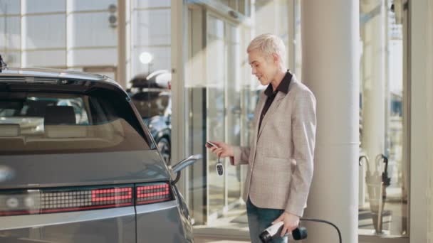 Strzał kobiety podchodzącej do swojego elektrycznego pojazdu, podłączającej go, żeby naładować na nowoczesny parking. Nowoczesny biznes kobieta łączy kabel do jej nowego samochodu elektrycznego, szybkie ładowanie w centrum biznesu — Wideo stockowe