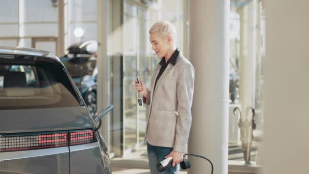 Eco elektrische auto concept. Een vrouw liep naar haar elektrische auto, plugde hem in om op te laden op de parkeerplaats. Zakelijke vrouw verbindt kabel met haar nieuwe elektrische auto, snel opladen in business center — Stockvideo