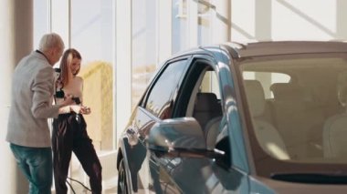 Çevre dostu ulaşım kavramı. İki mutlu genç kadın ilk defa modern bir kuaför salonunda ya da ofiste elektrikli bir araba şarj ediyorlar. Eko elektrikli araba.