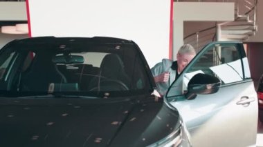 Neşeli genç bayan galeride yeni araba anahtarını gösteriyor. Yeni arabasının anahtarlarını alan yetişkin sarışın kadın, yeni arabasının anahtarını gösteren gülen beyaz kadının fotoğrafı. Araba kiralama kavramı.