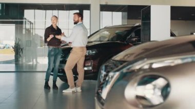 Orta yaşlı sarışın kadın gülümserken otomobil galerisindeki bir araba satıcısıyla yeni bir araba için ödeme oranlarını tartışıyor. Galeriden yeni araba alan bir kadın.