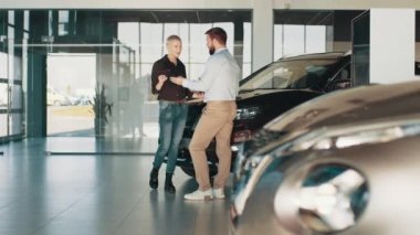 Pahalı satın alma kavramı. Elinde tabletle gülümseyen erkek araba satıcısı, araba almak isteyen siyah gömlekli bir kadın müşteriye araba tariflerinden bahsediyor. Araba kuaförü..