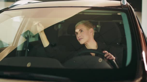 Beautiful female customer of showroom testing interior of new auto while sitting inside. Charming blond middle aged business woman fixing the rear view mirror while being ready to drive. — Stock Video
