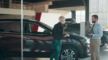 Araba galerisinde araba almak isteyen sarışın, kısa saçlı, iş kadını bir kadınla dolaşan ve araba özellikleri hakkında konuşan ciddi bir erkek araba satıcısı. İnsan ve ulaşım kavramı.