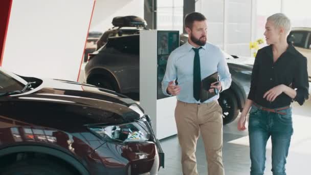 Car dealer and client talking about its performances in showroom. Attentive man car showroom consultant talking to woman client in car showroom vehicle salon dealership store motor show indoor. — Stock Video