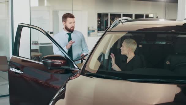 Szczęśliwy średni wiek szczupła blondynka biznes kobieta siedzi wewnątrz nowoczesnego samochodu podczas rozmowy z kompetentnym kierownikiem salonu. Wybór nowego pojazdu. Koncepcja drogich zakupów. Kobieta kupująca auto. — Wideo stockowe