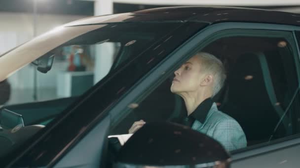 Shes very happy. Lady examining interior of luxury car while sitting inside. Beautiful business woman buying new car. Happy female customer buying new vehicle at modern showroom. — ストック動画