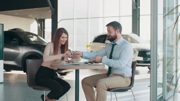 Compradores de coches. Cliente europea firmando papeles con vendedor en la tienda de concesionarios. Visitando concesionario de coches. Guapo gerente de ventas está sonriendo mientras hermoso cliente está firmando papeles — Vídeos de Stock