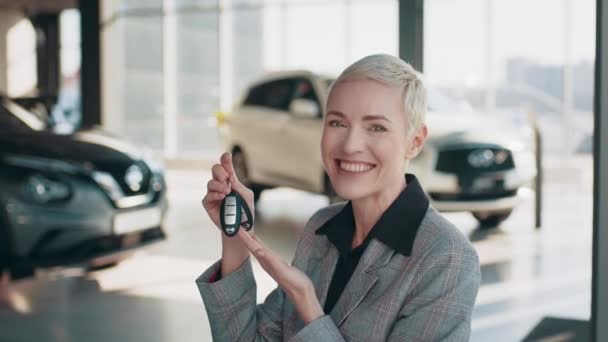 Krásná kavkazská žena blond žena podnikání žena ukazující klíče od auta po zakoupení nového drahého auta v prodejně automobilů. Profesionální žena prodejce v prodejně aut — Stock video