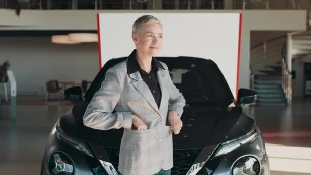 Θετική γυναίκα σε smart casual ρούχα χαμογελώντας για την κάμερα και επιδεικνύοντας τα κλειδιά, ενώ στέκεται κοντά σε νέο όχημα στο showroom. Ελκυστικό κορίτσι με κλειδιά αυτοκινήτου. Γυναίκα που δείχνει το κλειδί για το νέο της αυτοκίνητο. — Αρχείο Βίντεο
