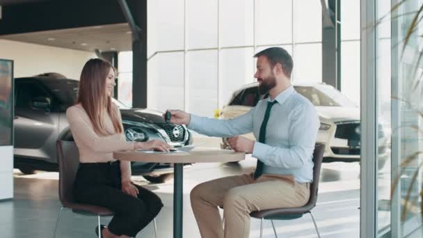 European female client signing papers with salesman in dealership store. Visiting car dealership. Handsome sales manager is smiling while beautiful client is signing papers and gets the keys — Vídeos de Stock