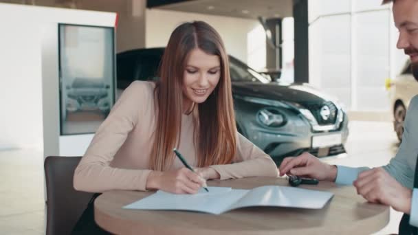Otomobil galerisindeki bayanla yeni araba imzalama kağıtları alıyor. Galeride kadın müşteri evraklarını imzalıyor. Kontratı imzaladıktan sonra müşteriye arabanın anahtarlarını vermek — Stok video