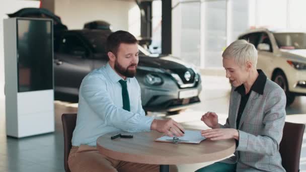 Giving the customer the car keys after signing the lease. Lady Buying New Car Signing Papers With Dealer Man In Auto Dealership Store. Female customer signing papers at the dealership showroom. — ストック動画