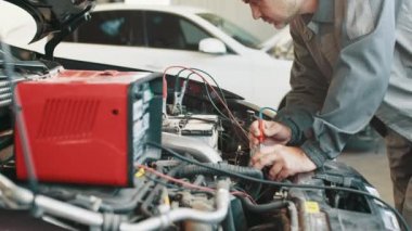 Araba tamiri servisinde çalışan profesyonel bir tamirci. Otomatik elektrikçi bir araba motoruna sorun çıkarıyor. Elektrikçi araba motoru üzerinde çalışıyor. Otomobil üzerindeki elektrik sistemi test ediliyor