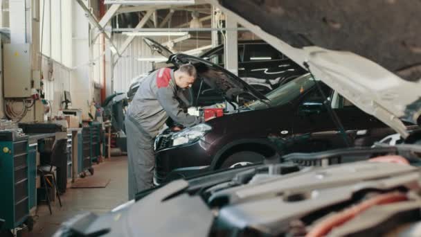 Mechanik v práci v garáži. Automobilový elektrikář má problémy s motorem. Elektrikář pracuje na automobilovém motoru. Mechanik opravuje auto na opravárenské stanici. Testování elektrického systému na automobilech — Stock video