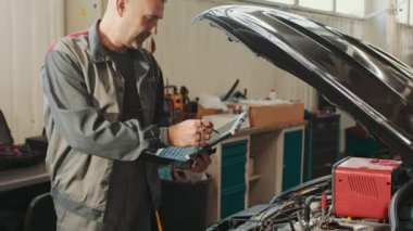Arabaların bilgisayar kontrolleri, tamirci erkek servis istasyonunda kaputu açık olan aracı tamir ederken dizüstü bilgisayar teknolojisi kullanıyor. Otomatik servis, onarım, bakım kavramı.