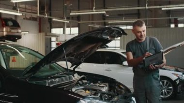 Aracın motor parçalarını tamir ve onarım için kontrol etmek ve tanı koymak için bilgisayarı kullanan araba tamircisinin portresi. Otomatik servis, onarım, bakım kavramı.