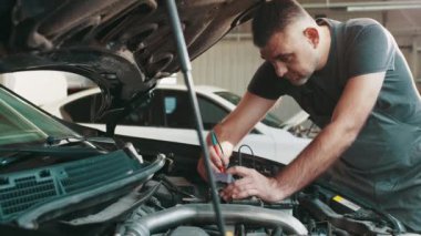 Tamirci elektrik tesisatını yeniliyor mu diye kontrol ediyor. Otomobil servisi atölyesi. Düzenli önleyici araba bakımı. Otomobil servisi, bakım konsepti. Elektrikçi bir araba motoruna sorun çıkarıyor.