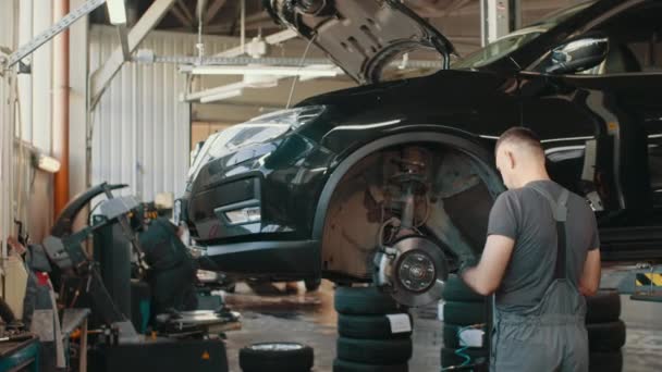 Sliding shot of auto mechanic checking SUV suspension of a lifted car. Experience car service technician working at the garage. Mechanic repairing car at his workshop. Car Service Employees Inspect — Stock Video