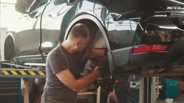 Selective focus disc brake on car, Car brake repairing in garage. Portrait Shot of a Mechanic Working on a Vehicle in a Car Service. Modern Clean Workshop. Car service, maintenance and people concept. — ストック動画