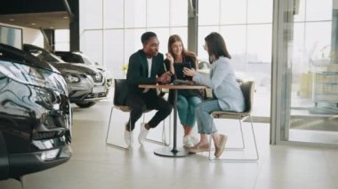 Elinde tabletle kadın otomobil satıcısı araba satın alma konusunda çok ırklı çifte profesyonel danışmanlık sağlıyor. İnsan kavramı, teknoloji ve bayilik. Kadın satıcı araba almaya yardım ediyor.