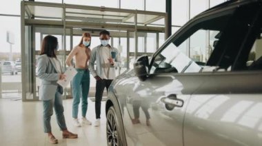 Yüzü maskeli Afrikalı Amerikalı bir adam modern salonda bayan yöneticinin yardımıyla yeni bir araba seçiyor. Ellerinde dosya olan beyaz bir menajer müşteriyi lüks bir araba yapmaya çalışıyor. Çeviri: teşekkür ederim.