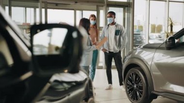 Yüzü maskeli Afrikalı Amerikalı bir adam modern salonda bayan yöneticinin yardımıyla yeni bir araba seçiyor. Ellerinde dosya olan beyaz bir menajer müşteriyi lüks bir araba yapmaya çalışıyor. Çeviri: teşekkür ederim.