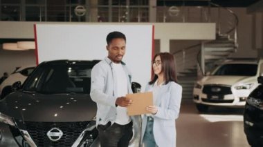 Araba galerisi, araba işi. Modern galeride erkek müşterilere danışmanlık yapan beyaz bir satış elemanı. Afro-Amerikalı adam bayilik merkezinde yeni bir araç seçiyor. Satma ve satın alma