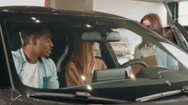 Modern otomobil merkezinde çok ırklı bir çiftle çalışan kadın satıcı. Mutlu Afrikalı adam ve beyaz kadın yeni araç seçerken yöneticilerine danışıyorlar. Çok ırklı bir çift ve satıcı.