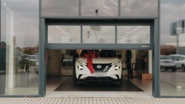 Modern oto kuaföründen çıkan büyük kırmızı yayı olan yeni beyaz lüks bir araba. Pahalı bir alıcı. Ulaşım, sürpriz ve satış kavramı. Modern salonda büyük kırmızı fiyonklu yeni beyaz lüks araba..