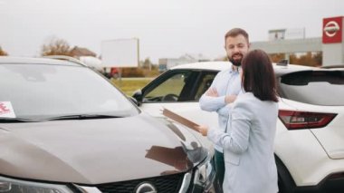 Kafkasyalı bir adam modern arabanın yanında kadın satıcıyla duruyor. Ön camında da satılık afişi var. Erkek müşteri, komedi çadırı satıcısının yardımıyla yeni bir araç seçiyor. Satıcı bayanla dışarıdaki araba hakkında konuşmak.