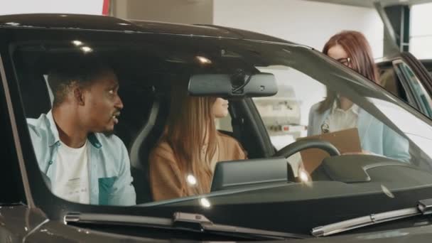 Female seller working with multiracial couple at modern auto center. Happy african man and caucasian woman consulting with manager while choosing new vehicle. Multi ethnic couple and saleswoman — ストック動画