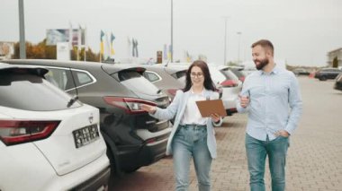 Satıcı kadın, bayilik merkezinin erkek müşterisine panoda bir şey gösteriyor. Mutlu sakallı adam, ön camında indirimli afişi olan modern bir araba alıyor. Adam satış elemanıyla dışarıda araba hakkında konuşuyor.