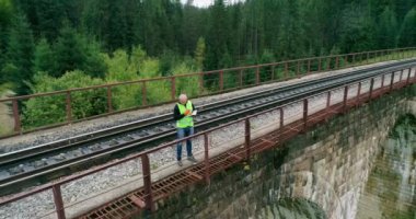 Demiryollarında havadan ateş edilmiş inşaat işçisi. Demiryolu mühendisi. Demiryollarında yürüyen ve rayları kontrol eden mühendis. İnsanlar demiryolunda yürür. Demiryolunda çalış. Nehir üzerindeki eski demiryolu köprüsü