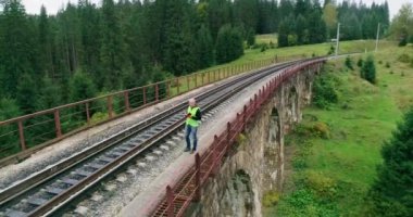 Demiryollarında havadan ateş edilmiş inşaat işçisi. Demiryolunda çalış. Nehir üzerindeki eski demiryolu köprüsü. Demiryolu mühendisi. Demiryollarında yürüyen ve rayları kontrol eden mühendis. İnsanlar demiryolunda yürür.