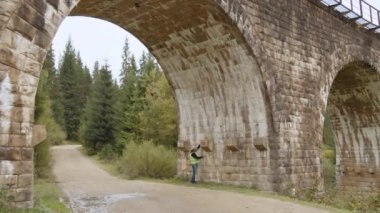 Kıdemli gri saçlı bir mühendis çok eski bir köprünün altında duruyor ve ölçümler yapıyor ve arızaları kaydediyor. Köprülerin yeniden inşası, antik demiryolu köprülerinin korunması. Mühendis müfettişi iş başında.