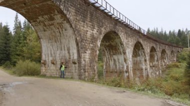 Köprülerin teftişi. Kıdemli gri saçlı bir mühendis çok eski bir demiryolu köprüsünün altında duruyor ve ölçümleri ve arızaları alıyor. Eski kemerli köprülerin yeniden inşası, kadim zamanların korunması