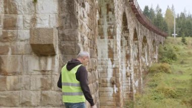 Eski binaları ve köprüleri restore etmek için kıdemli erkek mühendis. Mühendis laptopa veri yazıyor. Köprülerin yeniden inşası, antik demiryolu köprülerinin korunması. Mühendis müfettişi iş başında..