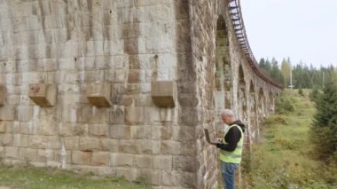 Eski binaları ve köprüleri restore etmek için kıdemli erkek mühendis. Mühendis veriyi dizüstü bilgisayara yazar. Köprülerin yeniden inşası, antik demiryolu köprülerinin korunması. Mühendis müfettişi iş başında.