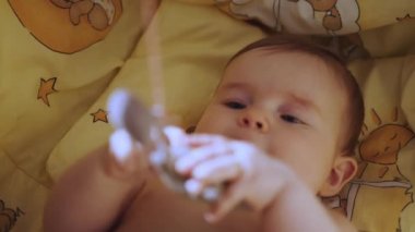 Top view cute newborn baby in bodysuit lying down in comfy mattress of cosy crib. Store ad of comfortable furniture for infants, healthy babyhood, child care concept. Baby trying reach the toys