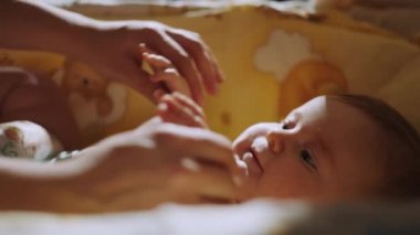 Little baby lying in crib and young mother sits about it. Happy family. Mother playing with him in crib. Concept of parenting, family happiness and baby development. Concept of parenting