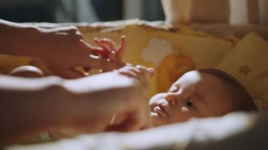 Close Up Footage of Newborn Baby Playing With Mothers Hand and Finger while Lying on the Back in Child Crib. Caucasian Neonate Toddler Bonding with Mom. Concept of Childhood, New Life and Parenthood