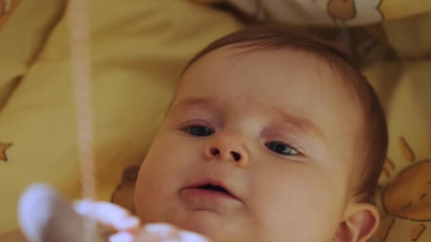 Baby care, first skills, learning to sit. Playful Portrait of a Caucasian Neonate Toddler Looking at Rotating Toys. A newborn baby lies in a crib and looks at a toy mobile. Child in the cradle. — Stockvideo